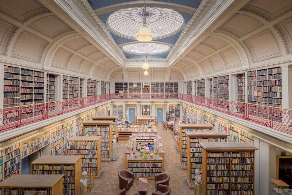 Young woman in a library looking thoughtfully through book shelves.
